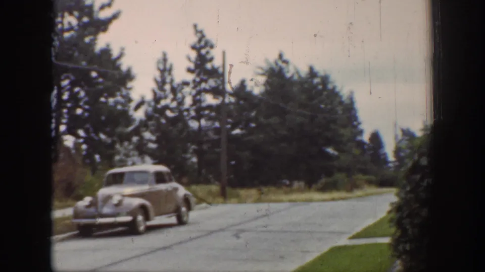 1939 Wyoming frame showing a single light-colored car moving along a tree-lined residential street in 8mm color footage.