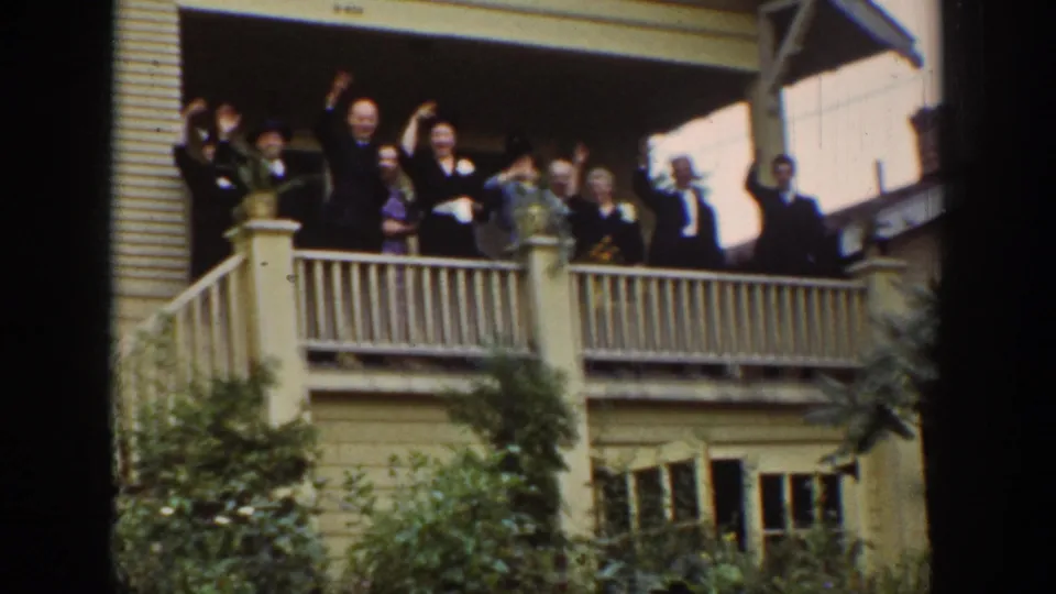 1939 Wyoming home-movie frame showing adults gathered on a porch, waving toward the camera or departing cars.