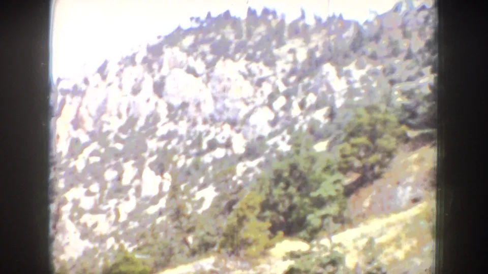 1939 Wyoming home-movie frame showing a bright rocky mountain slope with scattered trees and visible 8mm borders.