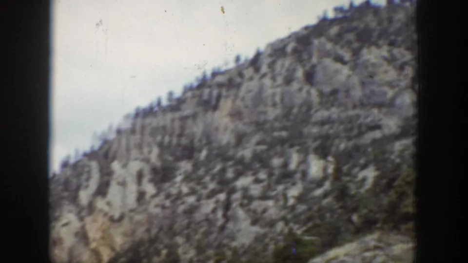 1939 Wyoming frame of a forested rocky mountain slope, softly rendered with pale sky and visible film texture.