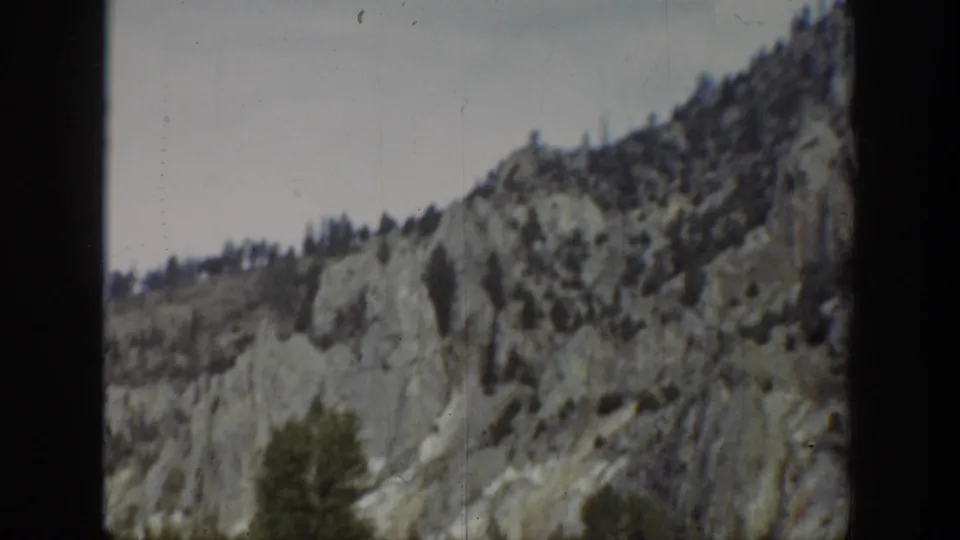 1939 Wyoming 8mm frame of a steep rocky hillside, scattered tree cover, and a small tree near the lower foreground.
