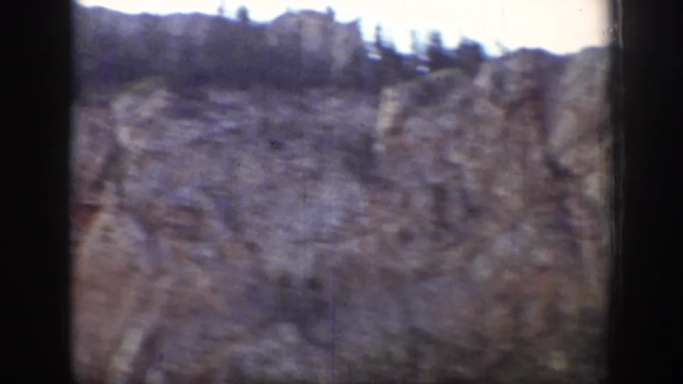 Wyoming 1939 home-movie frame showing a rocky cliff landscape, trees, and soft handheld exposure.