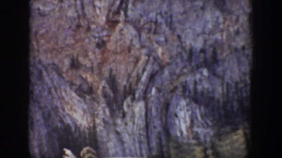 A handheld 8mm view lingers on the cliff face, with only a partial figure near the lower edge.