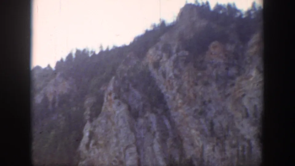 Handheld 8mm view of a Wyoming rocky outcrop rising toward evergreen trees, with faded color and visible film edge.