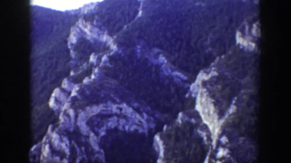 1939 Wyoming frame showing shadowed rocky formations and dense evergreen-covered slopes in a mountain ravine.