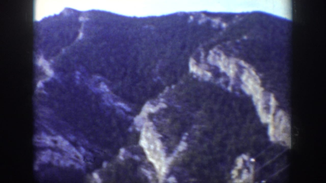 Forested mountain ridge with pale rocky cliffs and dark film borders.