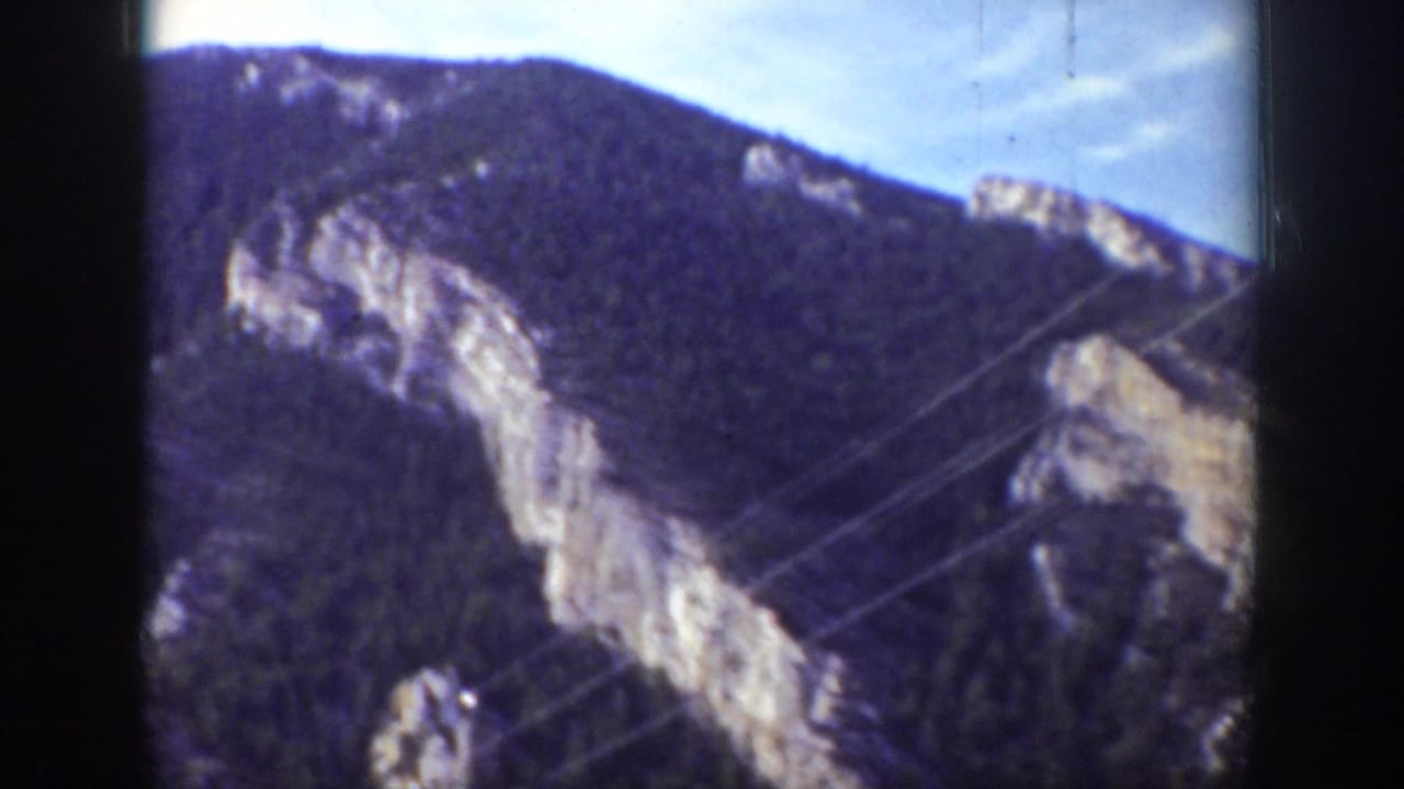 1939 Wyoming home-movie frame with rocky cliffs, dark forest, and diagonal telephone or utility wires.