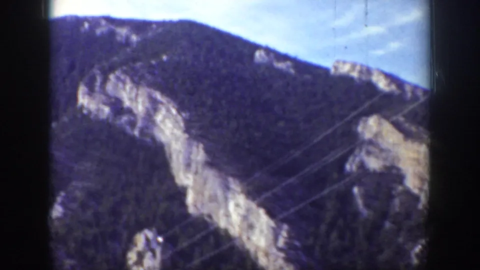 1939 Wyoming home-movie frame with rocky cliffs, dark forest, and diagonal telephone or utility wires.