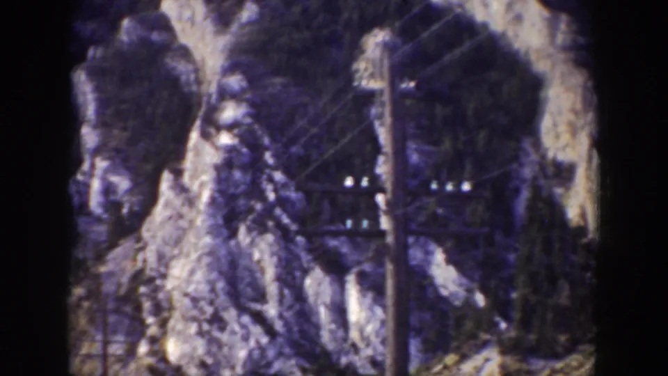 1939 Wyoming frame showing rocky cliffs, dark trees, utility wires, and a pole structure in the foreground.