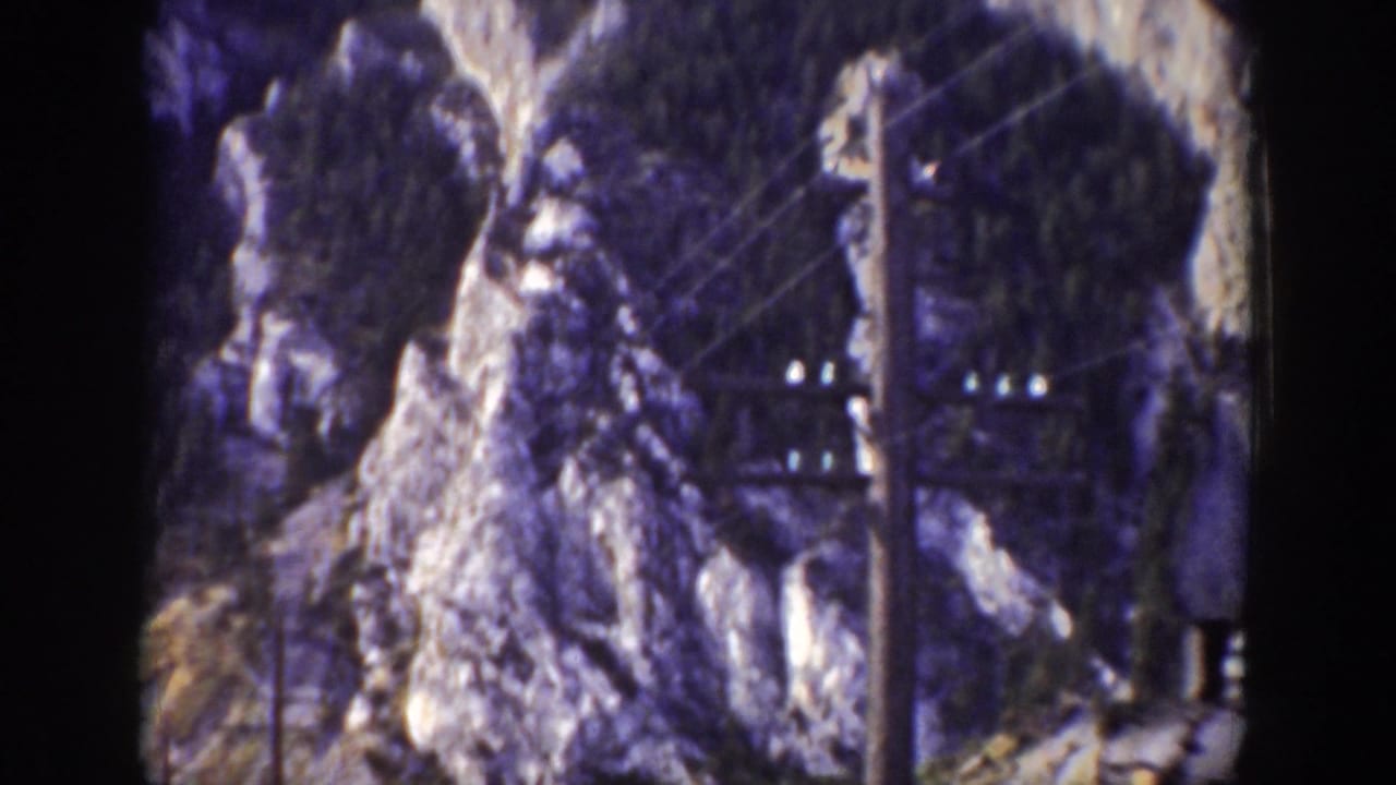 1939 Wyoming 8mm frame showing a rugged snow-dusted rock formation, utility pole, wires, and trackside ground before the train enters view.