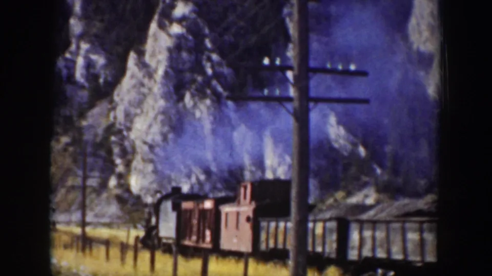 1939 Wyoming 8mm frame showing train cars, a steam plume, utility poles, and snow-dusted rock faces along the track.