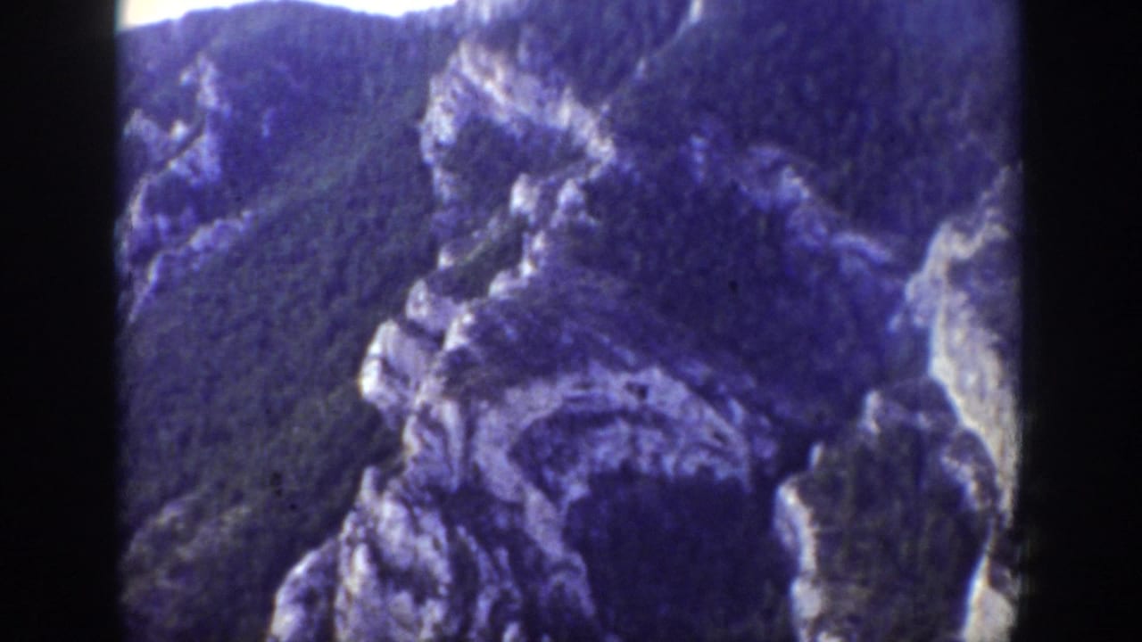 1939 Wyoming home-movie frame showing rugged cliffs, wooded mountain slopes, and a bright overexposed sky.