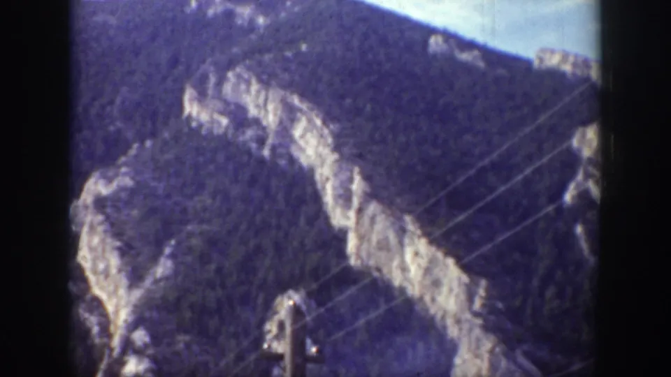 1939 Wyoming road-trip view with rocky forested slopes crossed by utility wires and a pole in the foreground.