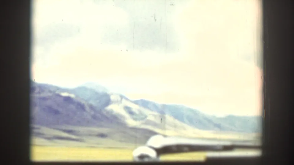 1939 Wyoming countryside viewed from inside a vehicle, with distant mountains, open land, window framing, and a nearby car shape.