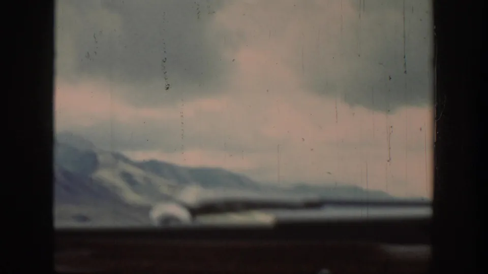 1939 Wyoming countryside seen through a car windshield, with mountain ridges, heavy clouds, and a dark dashboard edge.