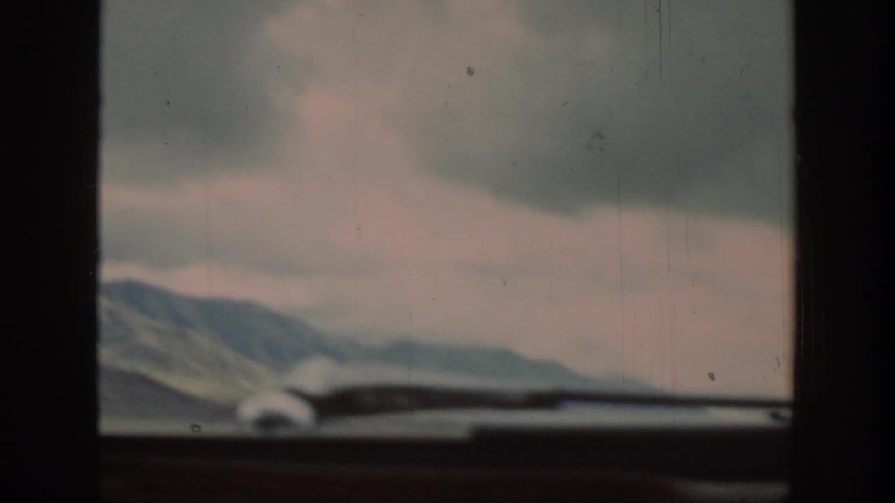 A 1939 Wyoming road-view frame shows distant mountains under gray clouds, partly obscured by the car windshield and dashboard.