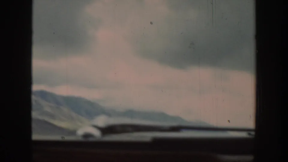 A 1939 Wyoming road-view frame shows distant mountains under gray clouds, partly obscured by the car windshield and dashboard.