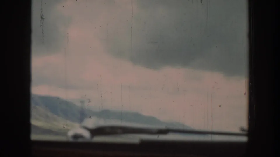 Wyoming mountain countryside appears beyond a car dashboard, with soft focus, overcast light, and visible 8mm film wear.