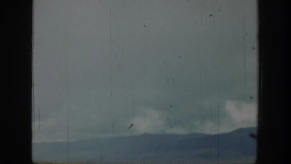 A distant Wyoming ridge sits under a cloudy sky, seen from within a car with dark windshield edges and aged-film texture.