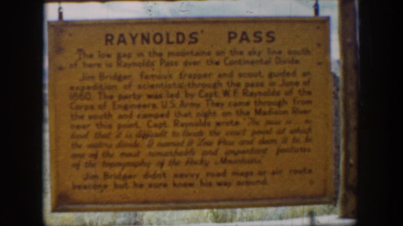 Soft 8mm frame of the Reynolds' Pass historical sign, with faded orange surface and dark lettering visible.