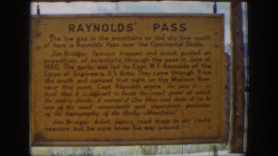 1939 home-movie still showing the Reynolds' Pass sign, with the text softened by focus and film grain.