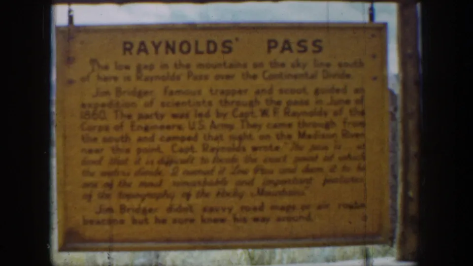 Final 8mm frame of the Reynolds' Pass historical sign in Wyoming, with faded color, grain, and minor scratches.
