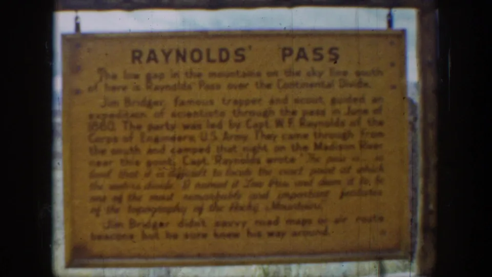 1939 Wyoming home-movie frame showing a weathered yellow Reynolds' Pass historical sign in soft 8mm focus.