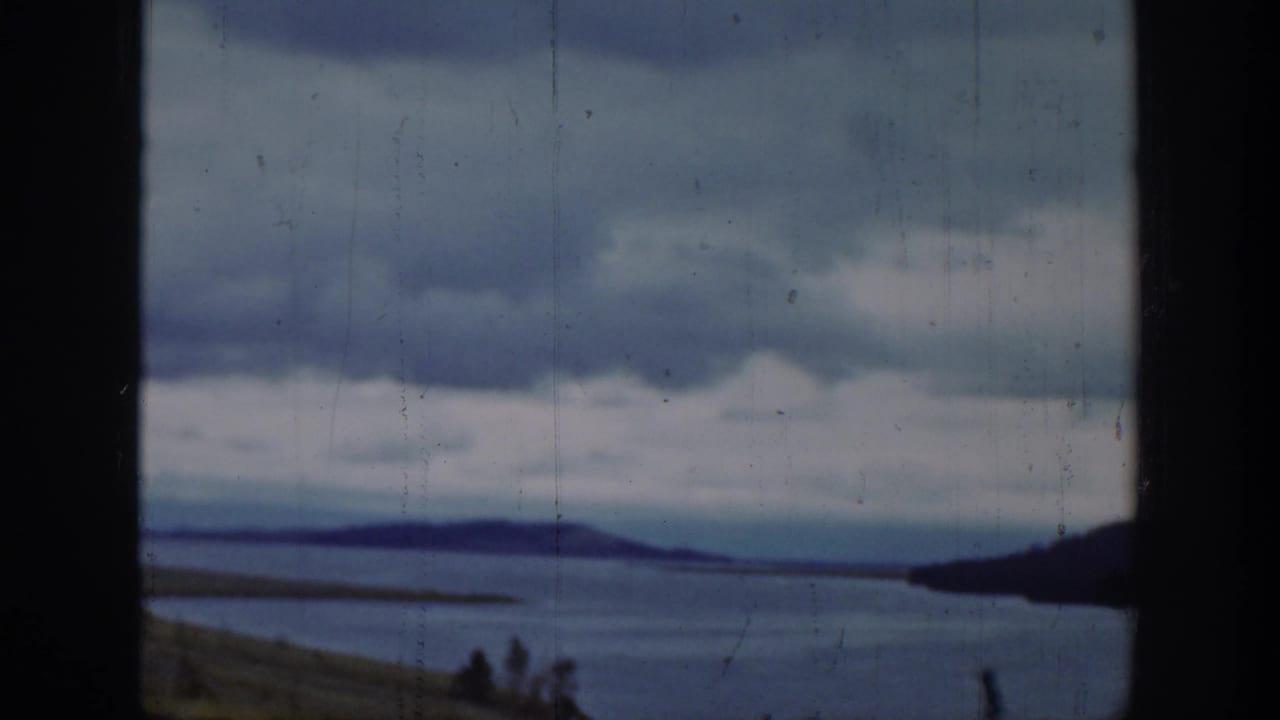 1939 Wyoming home-movie frame showing a broad lake, distant hills, cloudy sky, and dark vertical framing in the foreground.