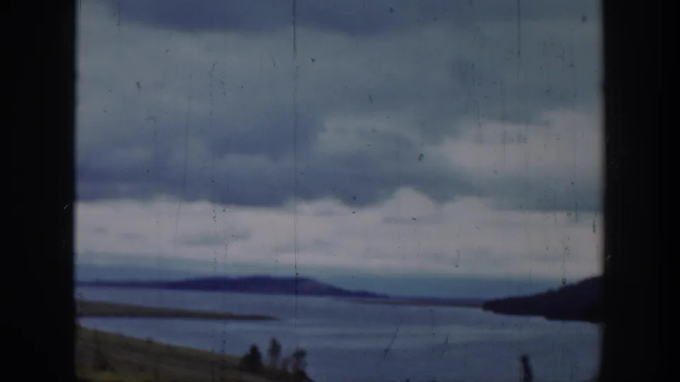 1939 Wyoming home-movie frame showing a broad lake, distant hills, cloudy sky, and dark vertical framing in the foreground.