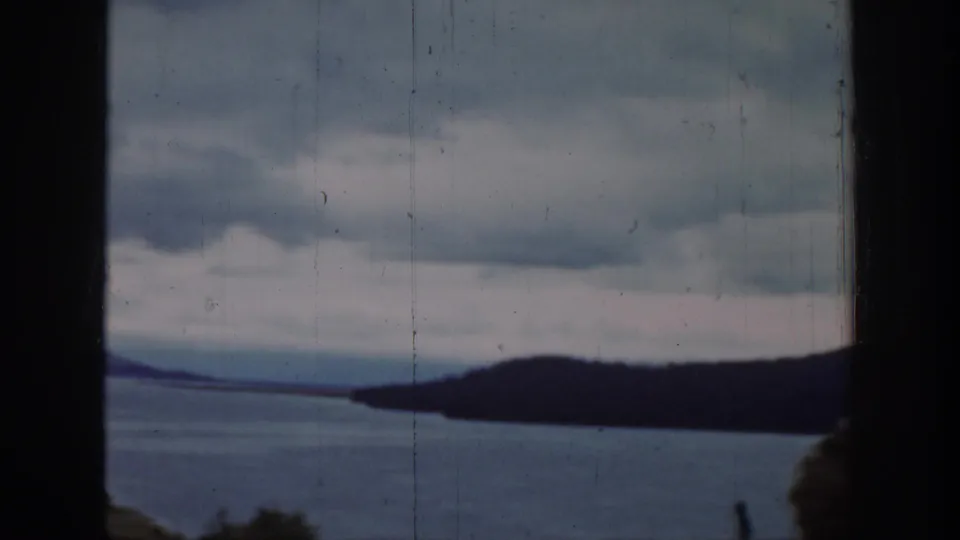 1939 Wyoming scenery with water, a dark wooded headland, layered clouds, and a central dark frame edge from the camera position.