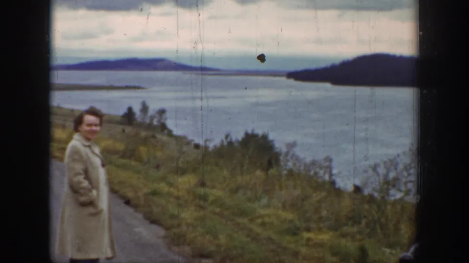 The 1939 Wyoming 8mm frame shows a woman near a rural road edge, facing the camera with riverbank vegetation and distant water behind her.