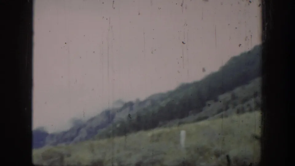 Blurred moving-vehicle view in Wyoming, 1939, looking across grassland toward low hills and a pale roadside post.