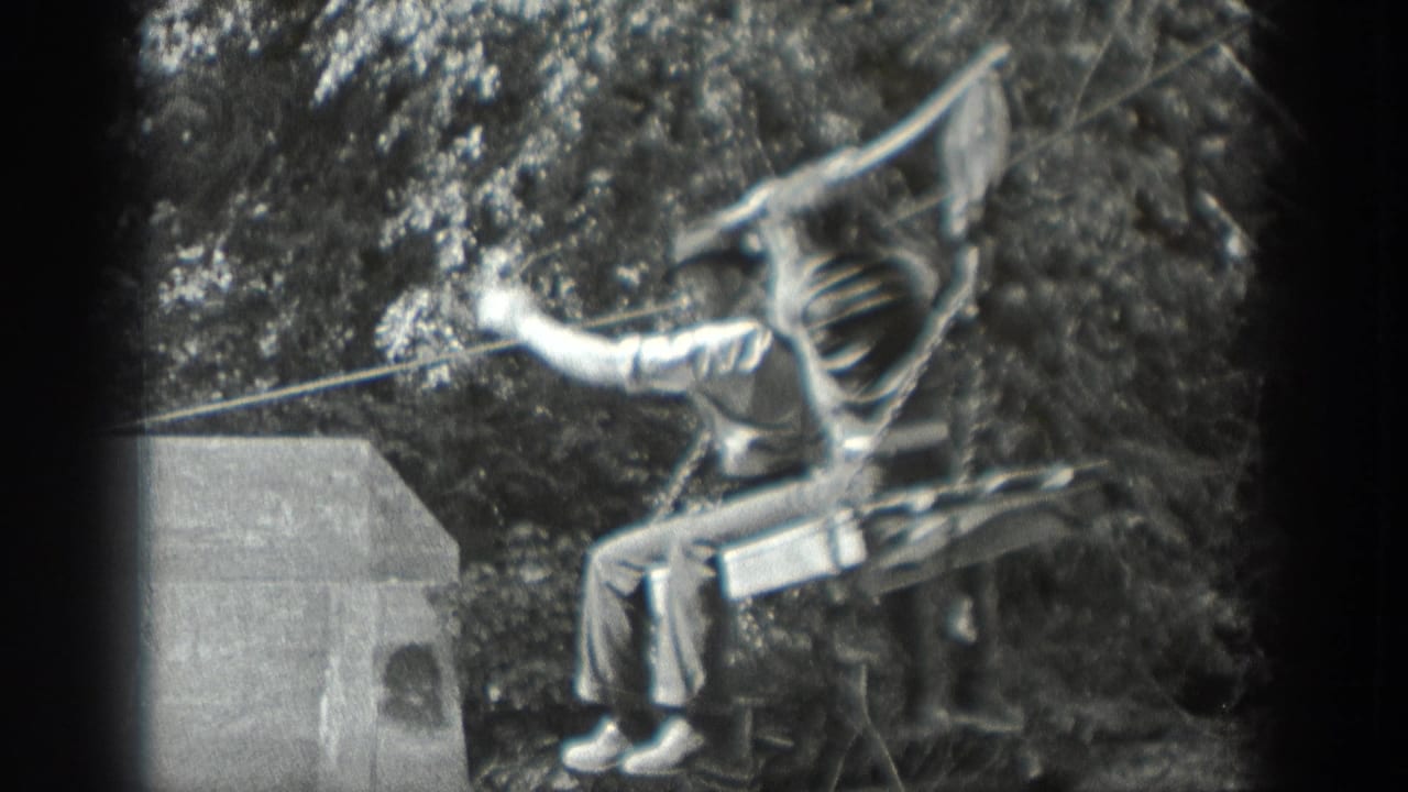 1940 Washington 8mm frame showing a young man riding a simple zip-line seat beside trees and a small concrete structure.