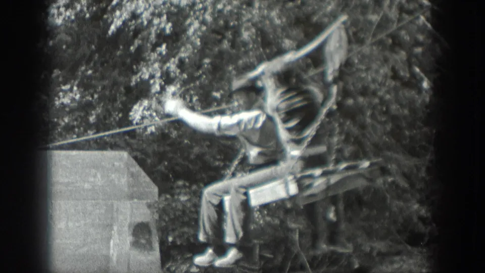 1940 Washington 8mm frame showing a young man riding a simple zip-line seat beside trees and a small concrete structure.