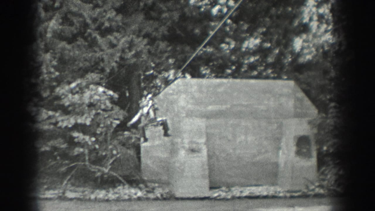Two figures remain on a rope beside a concrete structure with trees and riverbank nearby.