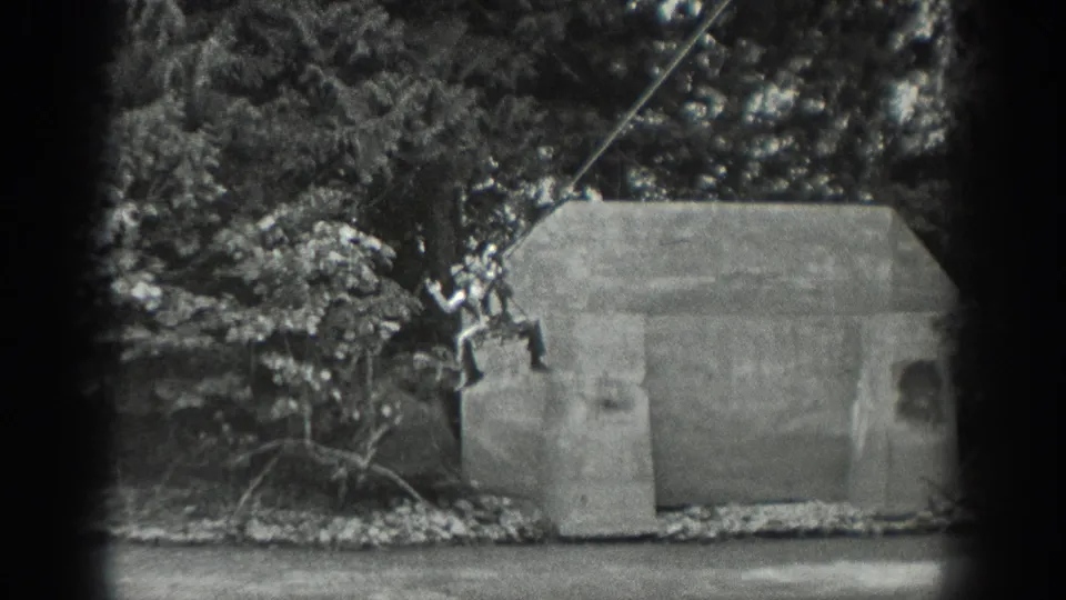 1940 Washington 8mm frame where a person appears suspended on a rope beside a small concrete structure near water and trees.