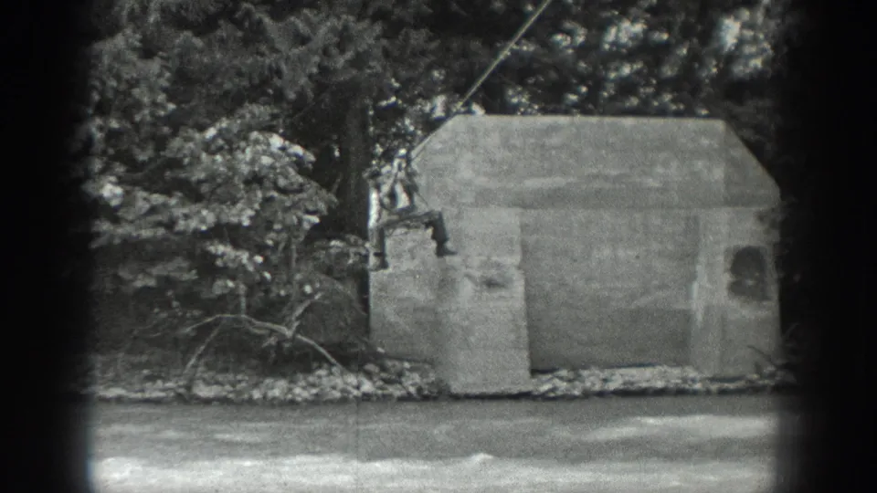 1940 Washington home-movie frame showing a distant figure near a rope and concrete riverside structure, with water and trees surrounding the scene.