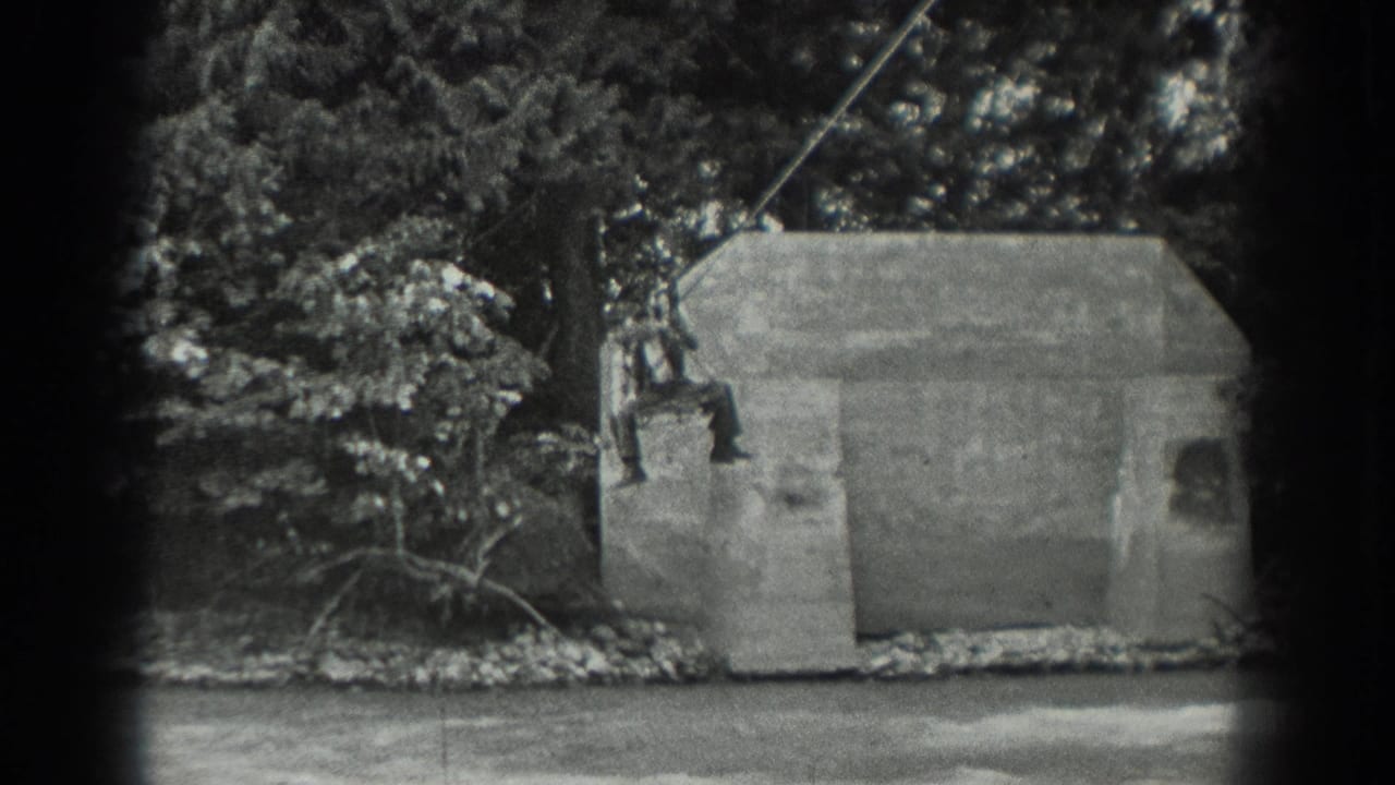 Man on a suspended cable passes in front of a concrete structure by the water.
