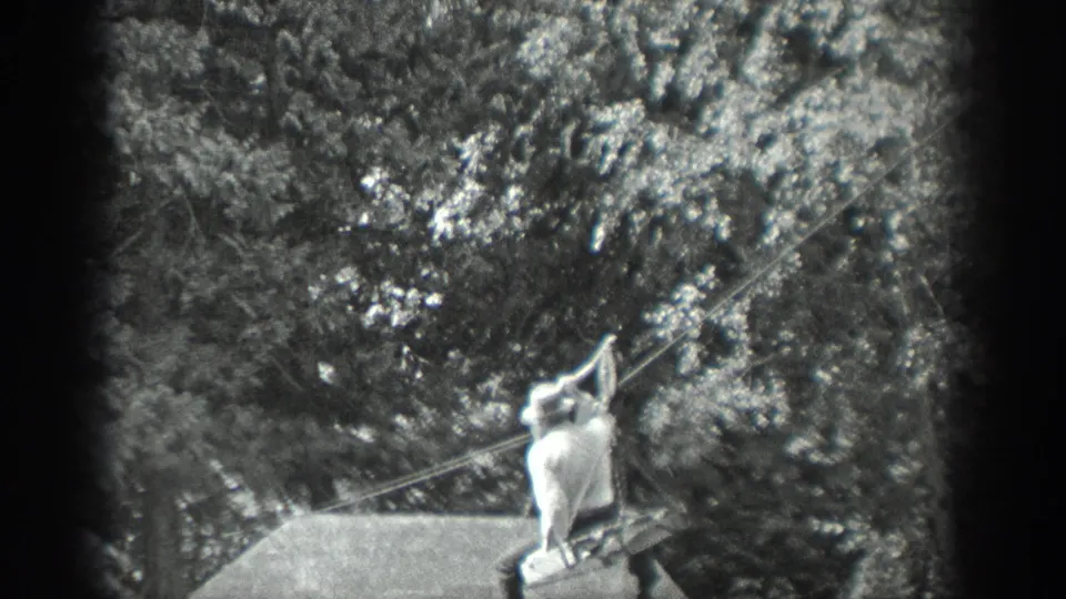 The cable rider appears farther across the wooded Washington waterway, seated under the line in soft black-and-white 8mm footage.