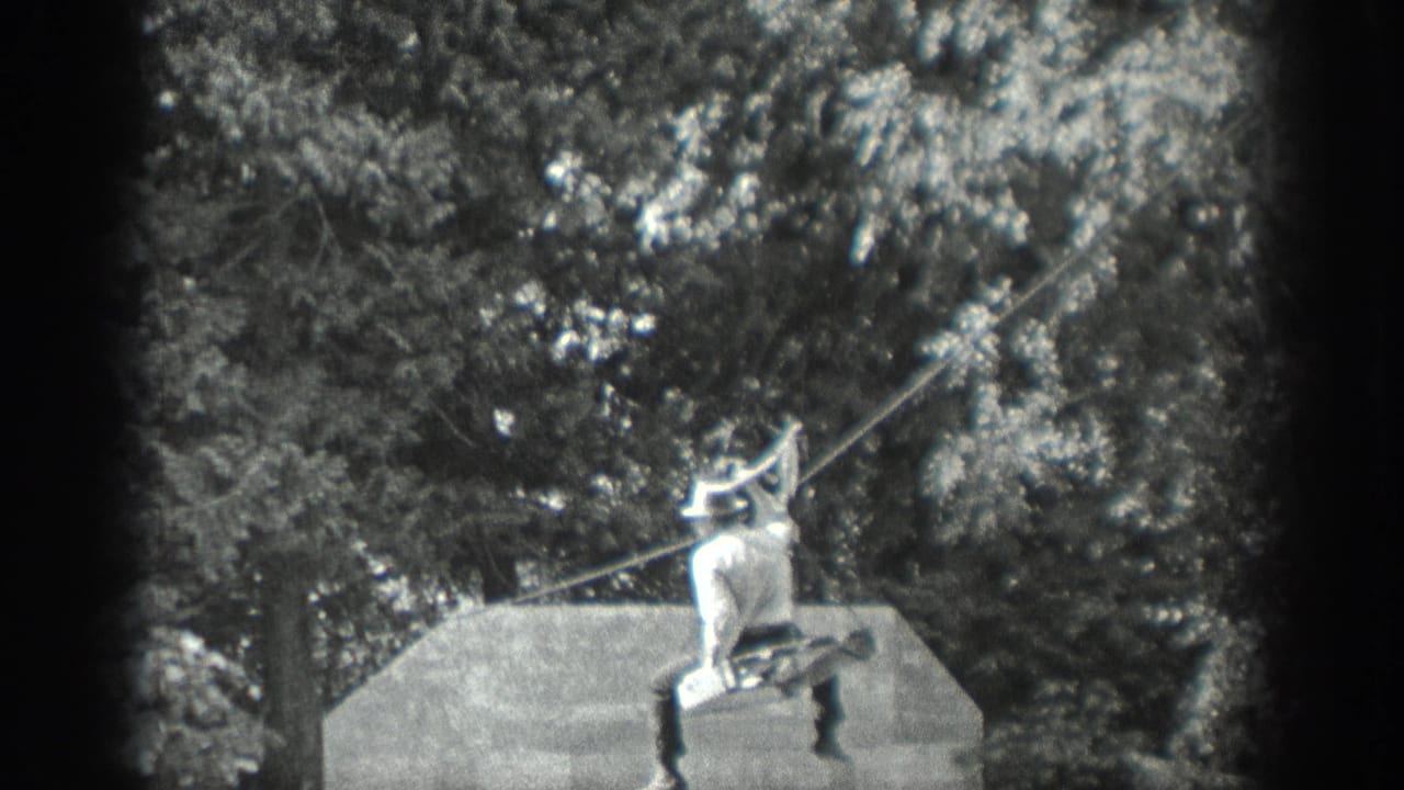 In Washington home-movie footage from 1940, a man in light clothing and a hat holds a taut line beside a platform in a wooded setting.