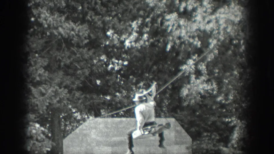 In Washington home-movie footage from 1940, a man in light clothing and a hat holds a taut line beside a platform in a wooded setting.