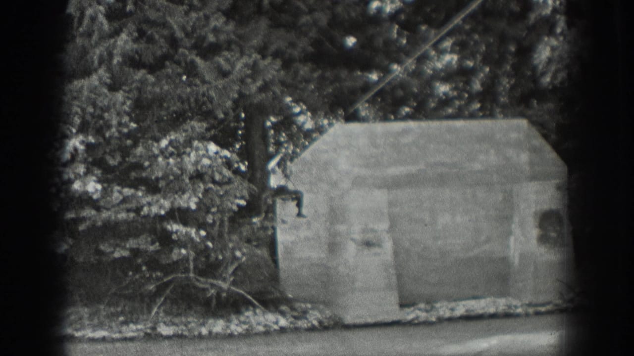 1940 Washington 8mm frame showing a concrete streamside structure, wooded background, water, and a cable line before the man enters view.