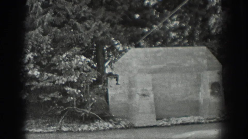 1940 Washington 8mm frame showing a concrete streamside structure, wooded background, water, and a cable line before the man enters view.