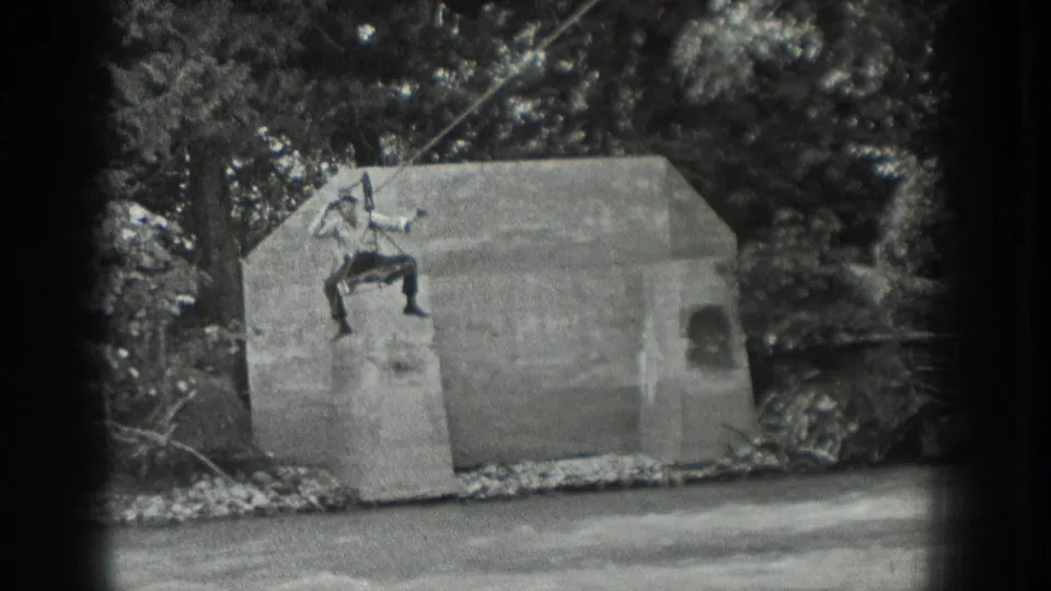 Final 1940 Washington frame showing the man with arms out on the cable above the concrete structure, stream, and wooded bank.