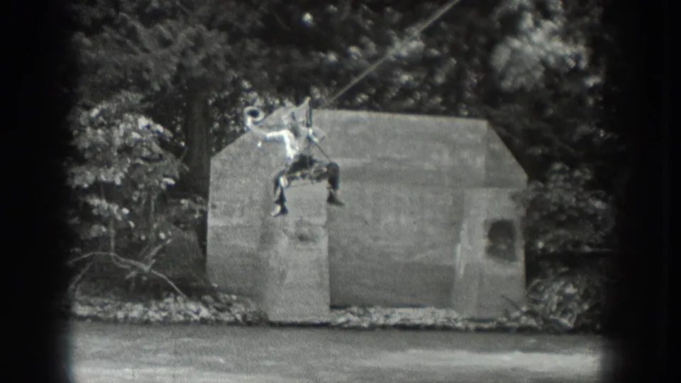 1940 Washington 8mm frame showing a man on a cable-suspended seat near concrete supports and trees.