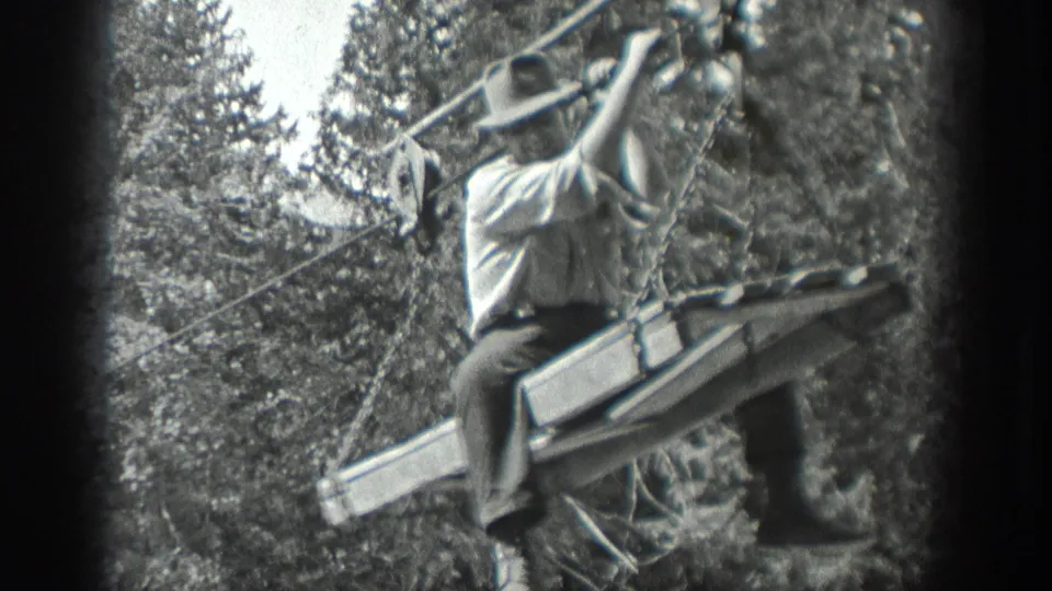 Closer 1940 Washington home-movie view of a man riding a wooden platform suspended from cables among trees.