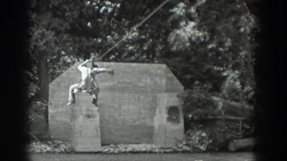 1940 Washington 8mm frame showing a man on a cable ride above a concrete structure, surrounded by wooded foliage.