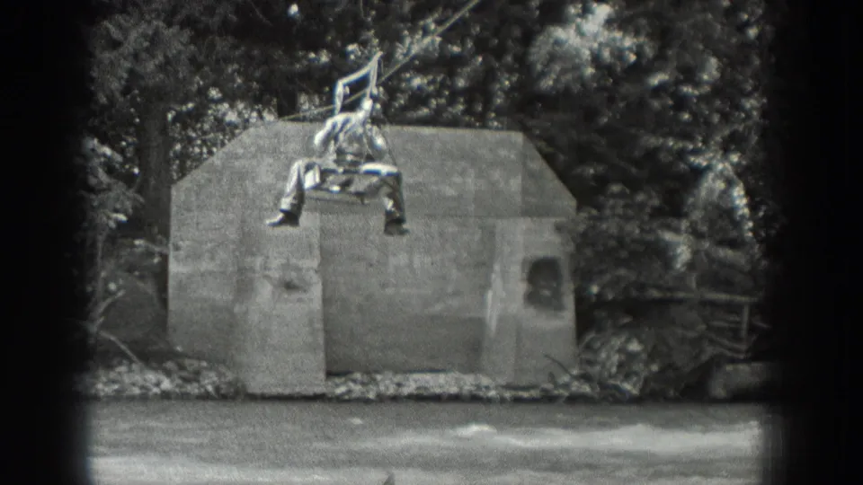 An adult man sits on a small suspended platform over the river, moving along a rope or cable system in 1940 Washington home-movie footage.