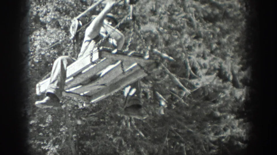 A closer black-and-white frame shows the adult man seated on a wooden pulley platform as it moves along cables near dense trees in Washington.