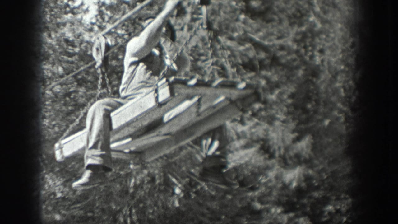 Black-and-white 8mm frame from Washington, 1940, showing a man seated on stacked logs or boards beside a cable in the woods.